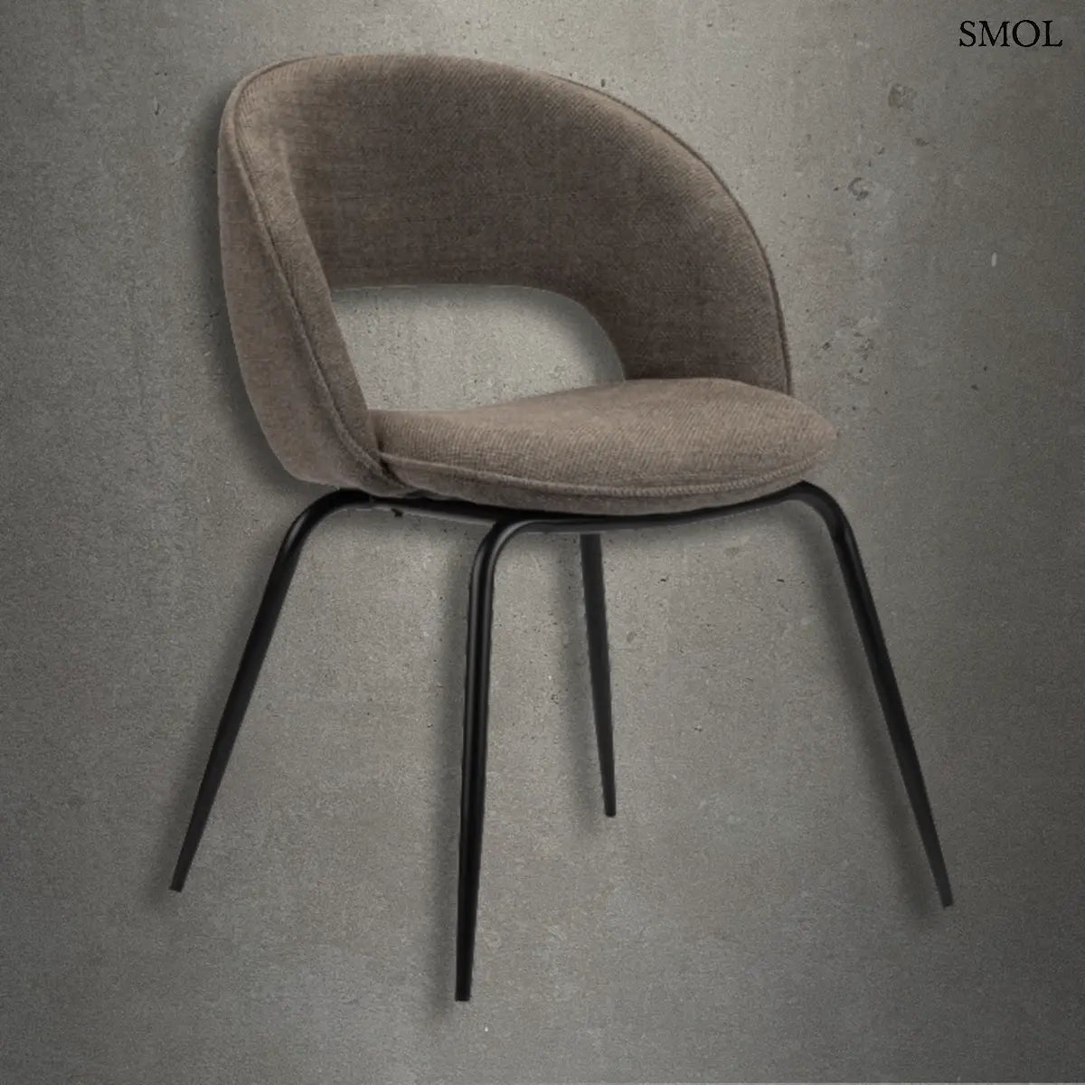 Modern, íves háttámlájú étkezőszék taupe színű szövettel és vékony, fekete fém lábakkal, minimalista betonfal előtt.