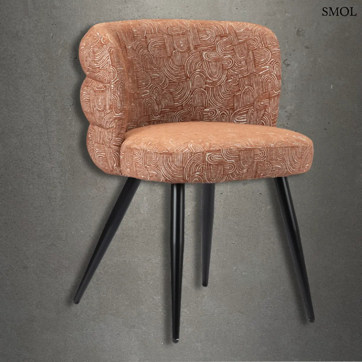 Modern, kagyló formájú étkezőszék terrakotta színű, absztrakt mintás kárpittal és karcsú, fekete fémlábakkal, beton hatású háttér előtt.