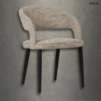 Modern, kerekített háttámlájú TUSK COCO étkezőszék bézs színű, texturált szövet kárpitozással és karcsú, fekete fém lábakkal, szürke betonhatású háttér előtt.