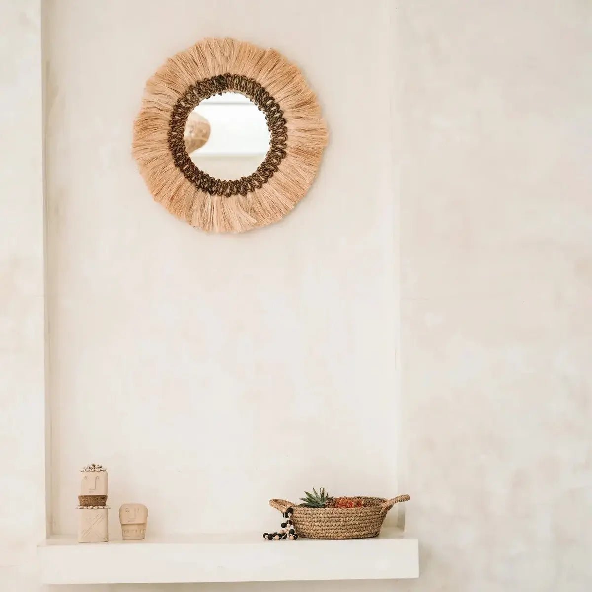Kerek falitükör natúr fű díszítéssel és rojtos boho kerettel, falon, szobrokkal és kosárral
