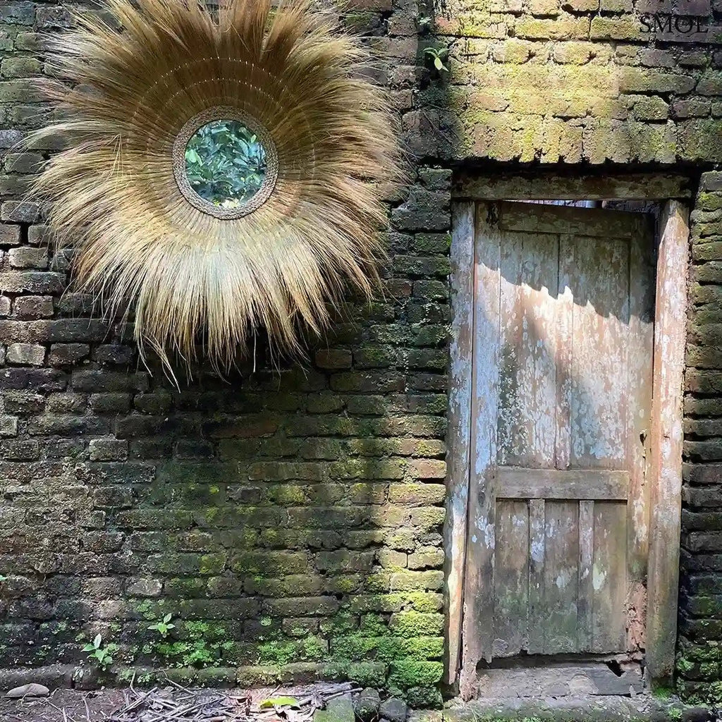 Kézzel font, kör alakú falitükör természetes szárított fűből, napsugár formájú szálakkal és mélyített üvegfelülettel, ajtó mellett