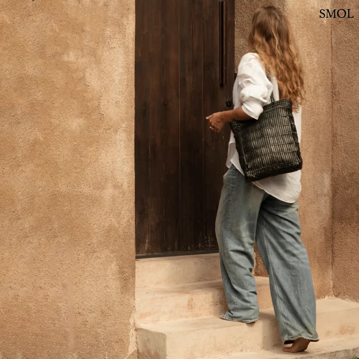 Kézzel fonott fekete bőr táska elegáns textúrával, hosszú vállpánttal és tágas kialakítással, női alakon