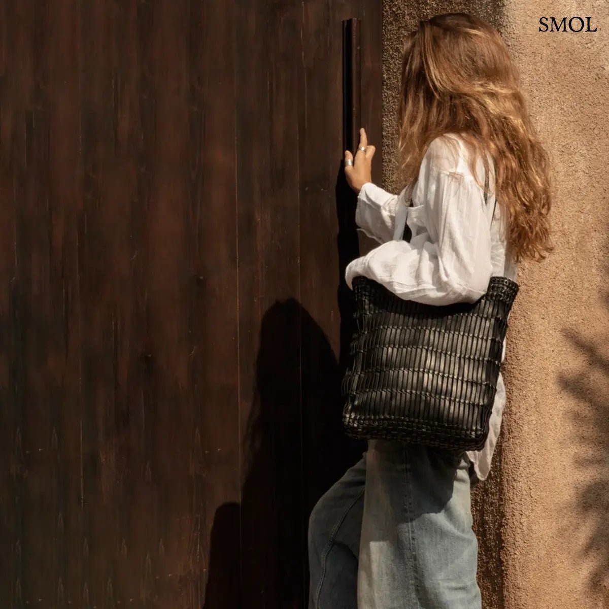 Kézzel fonott fekete bőr táska elegáns textúrával, hosszú vállpánttal és tágas kialakítással, női vállon