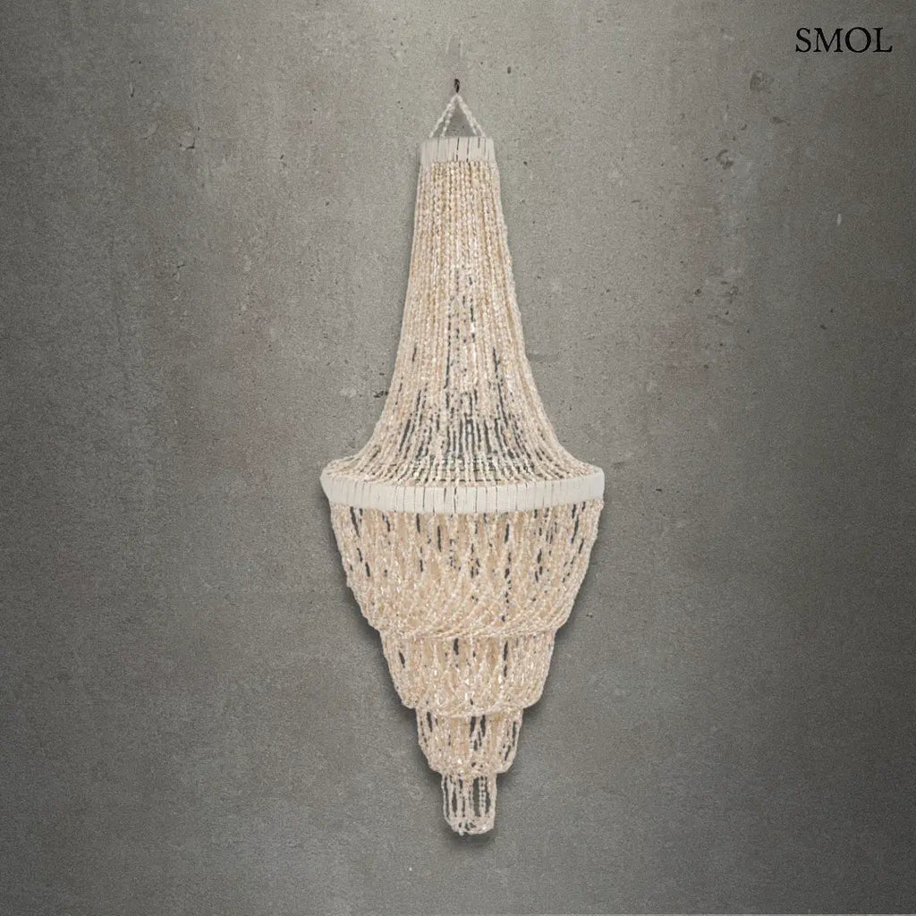 Lépcsőzetes kialakítású, fehér kagyló csillár natúr bojtos díszítéssel és fém vázzal, szürke háttérrel