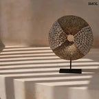 Natúr fehér kagylókból készült, kör alakú kagyló dekoráció fekete fémállvánnyal natúr háttérrel