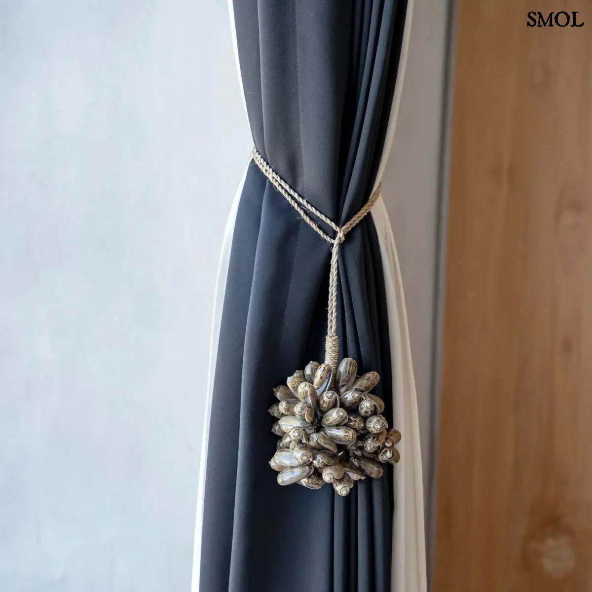 Barna kagyló függődísz, kézműves bojt formában, natúr kötélre akasztva függönyön