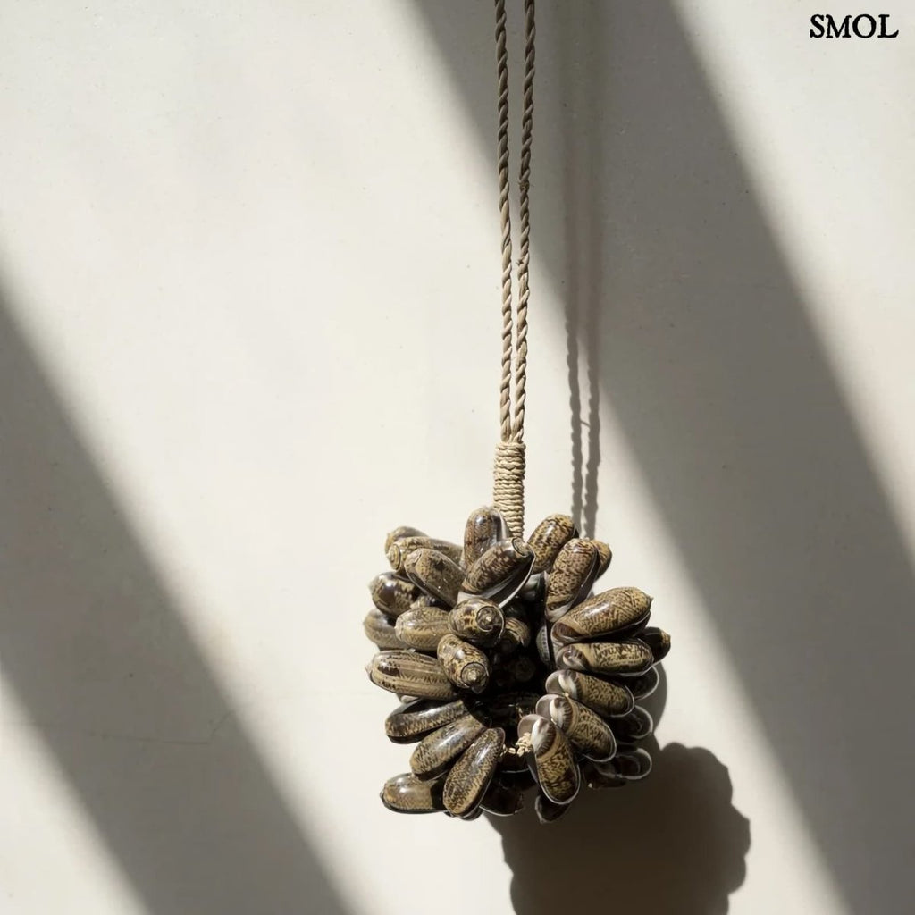 Barna kagyló függődísz, kézműves bojt formában, natúr kötélre akasztva falnál