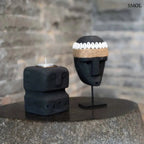 Fekete kő mécsestartó, kézzel faragott stilizált arc motívummal, Sumba-szigeti homokkőből, fekete maszkkal lerakóasztalon