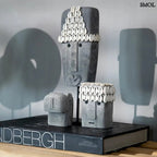 Kézzel faragott homokkő szobor kagylódíszekkel, fekete fém talapzaton, szürke szobrokkal, könyvön