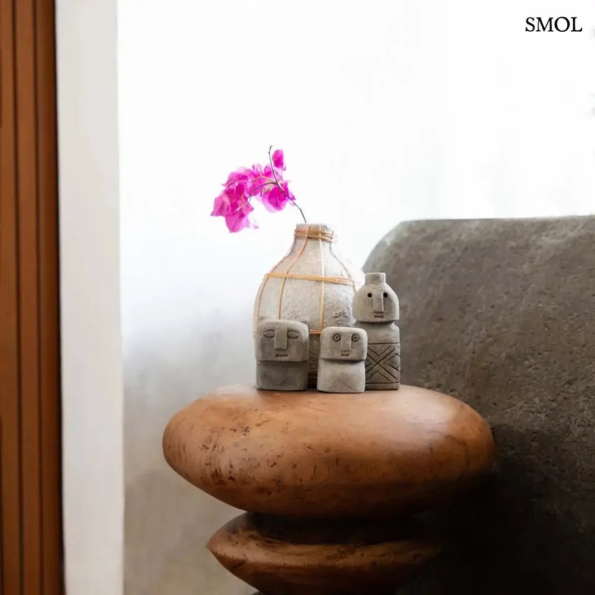 Kézzel faragott szürke homokkő szobor Sumba szigetéről, minimalista arcvonásokkal és hegyes fülekkel, kisasztalon, vázával