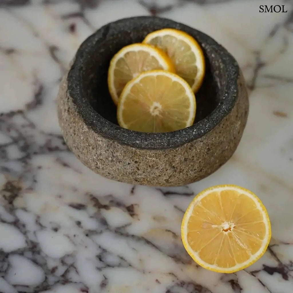 Rusztikus fekete lávakő tál kívül durva, belül csiszolt textúrával, természetes vulkanikus kőből, citrommal