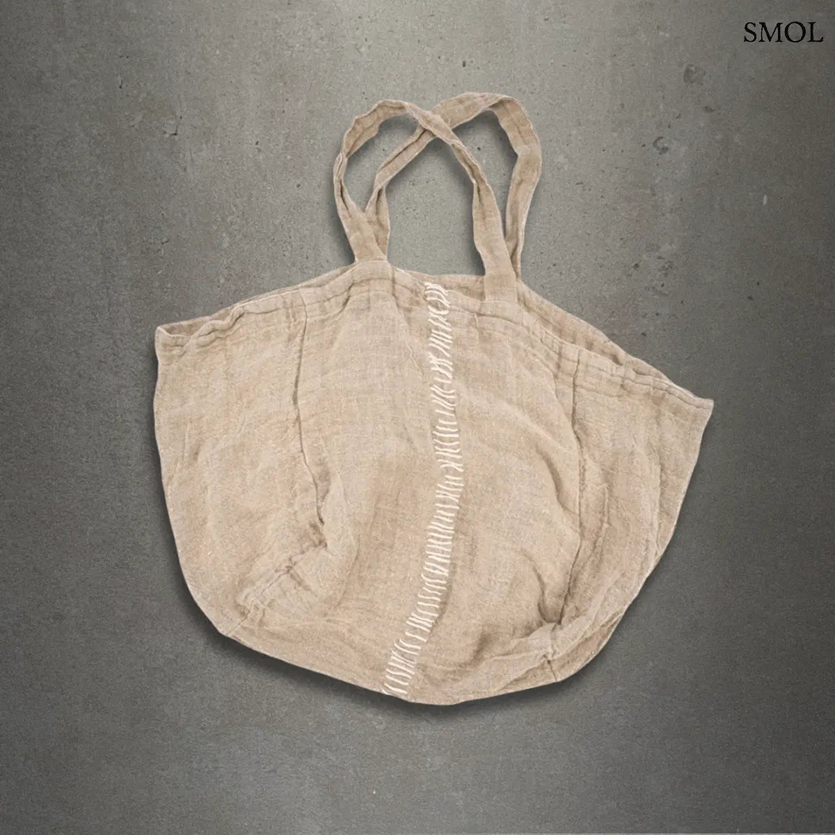 Természetes színű, rusztikus textúrájú lenvászon táska fehér, kézzel varrott hímzéssel díszítve, tágas shopper fazonban, szürje háttérrel