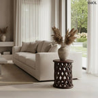 Sötét tónusú, kézzel faragott mangófa lerakóasztal és ülőke áttört rombusz mintázattal és sima, kerek fedőlappal, kanapé mellett