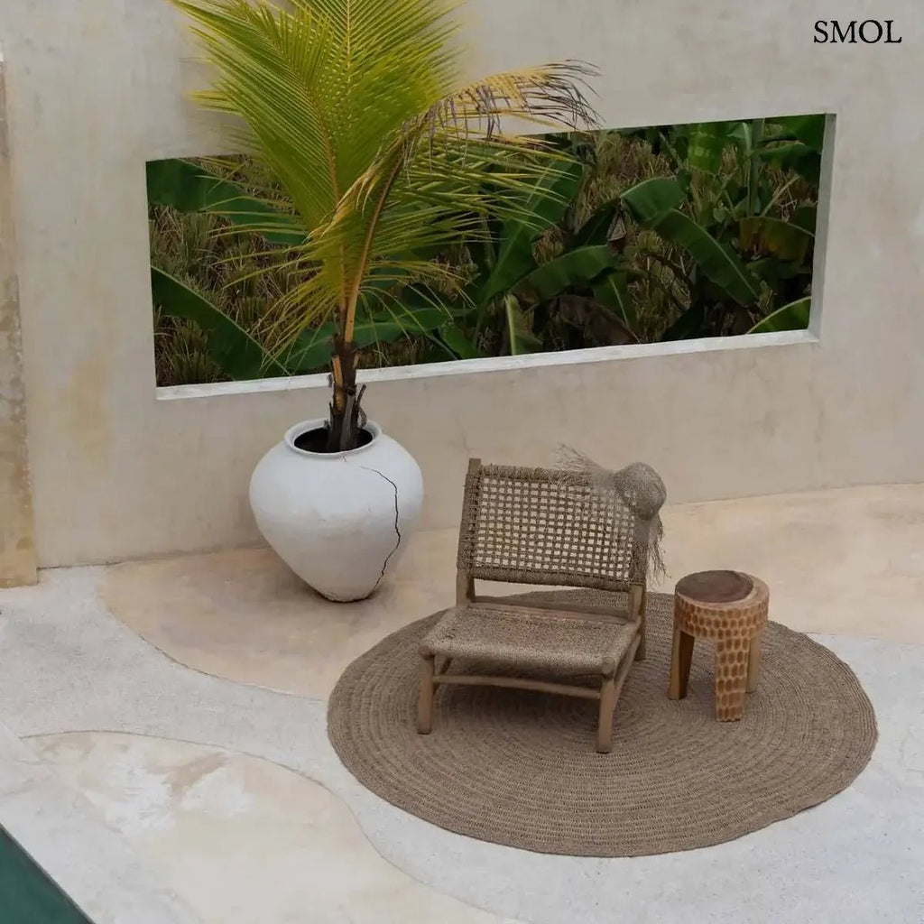 Rusztikus lerakóasztal és ülőke kézzel faragott tömör suar fából, háromlábú kivitelben és természetes fa erezettel, teraszon, fotellel, szőnyeggel