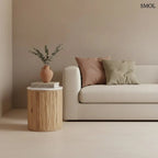 Henger alakú MALACCA lerakóasztal fehér márvány asztallappal és függőlegesen mart, natúr mangófa talppal, kanapé mellett, vázával és könyvekkel