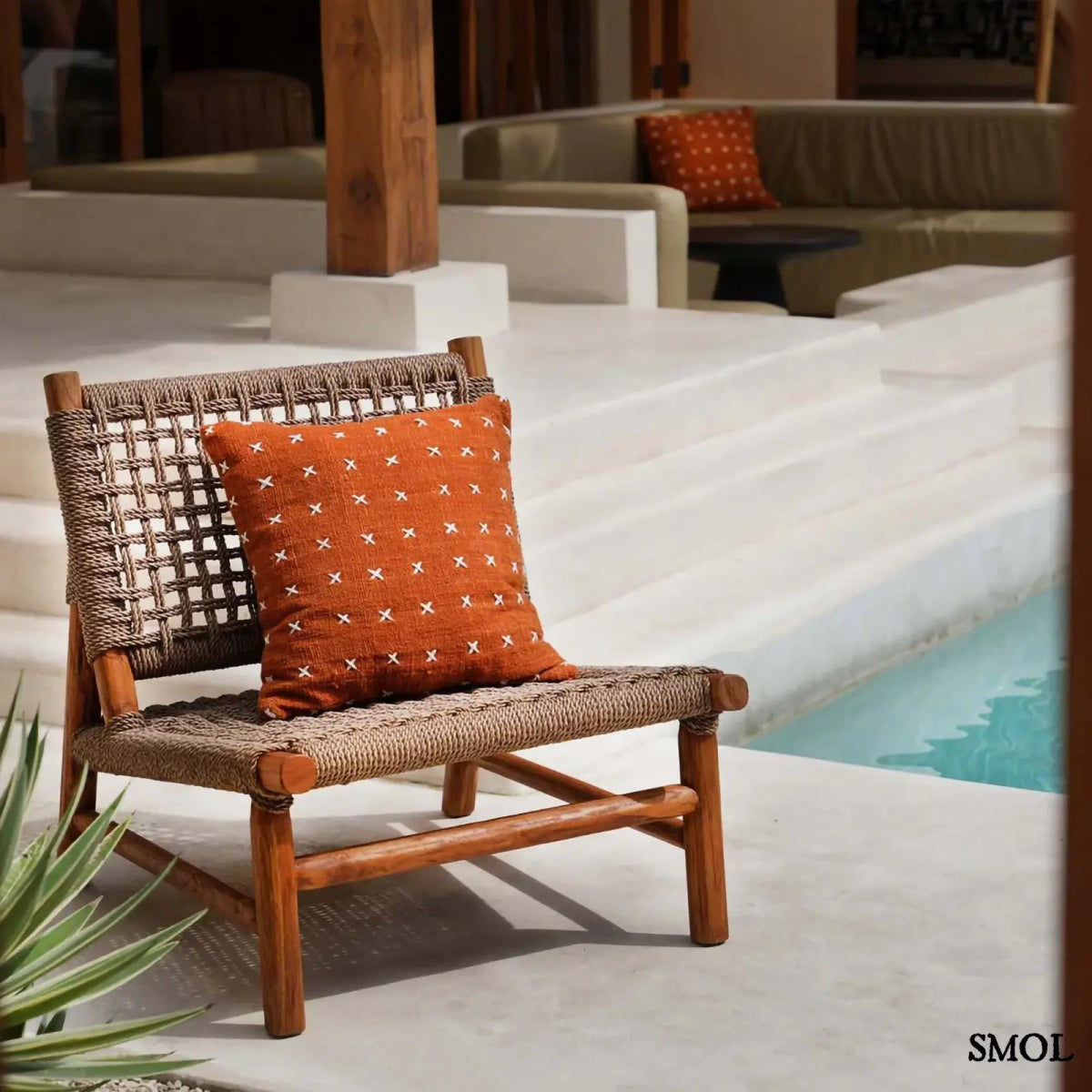 Pamut díszpárnahuzat, élénk terrakotta színben, sűrűn elhelyezett, kézzel varrott fehér kereszt mintákkal, teraszon, fotelben