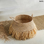 Raffia tárolókosár natúr színben, rojtos boho díszítéssel, padlón