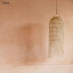 Kézzel szőtt, natúr színű, hosszúkás rattan függőlámpaernyő, alján lelógó, organikus szálakkal, bézs háttérrel