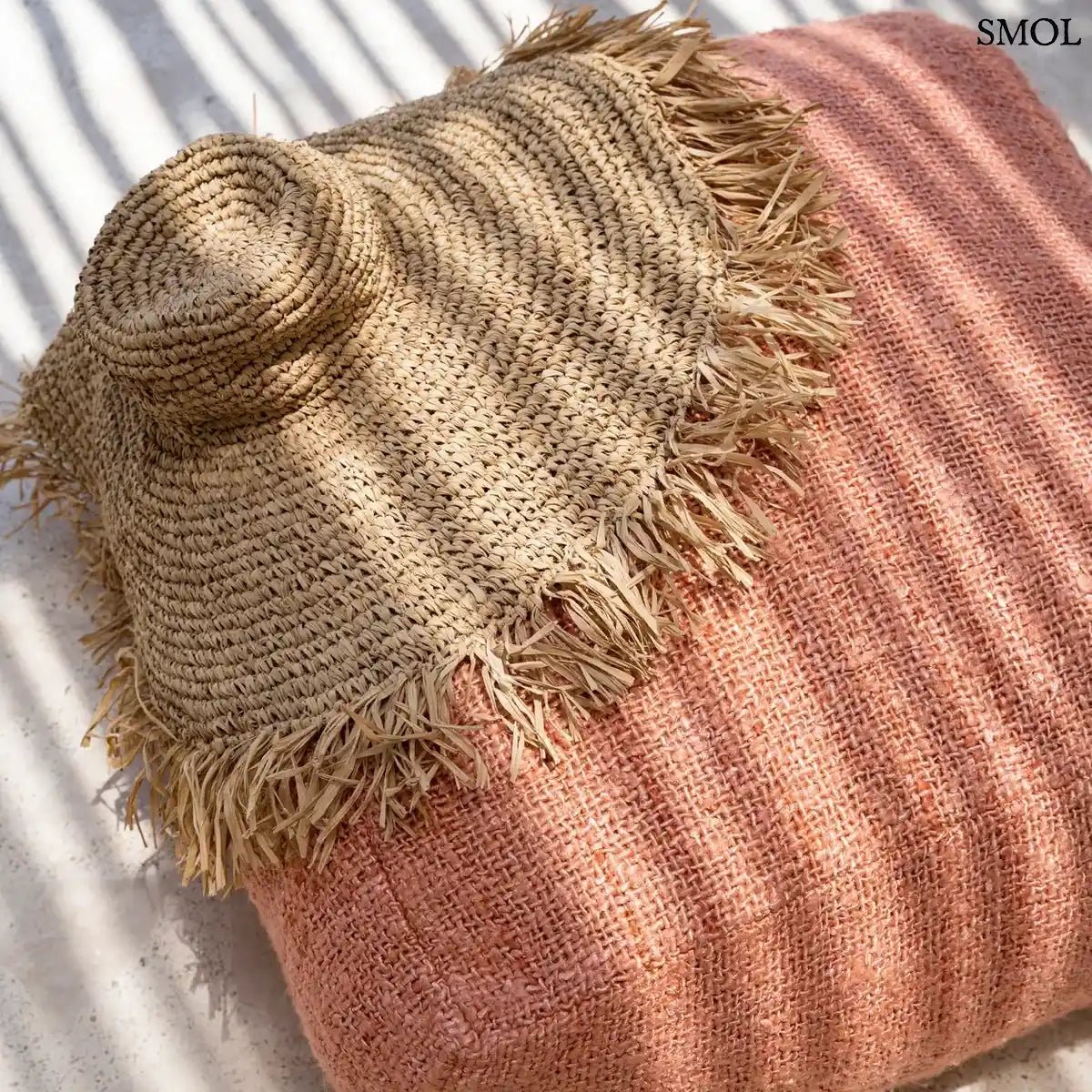 Kézzel szőtt, natúr barna szalmakalap széles, rojtos karimával, lazacszínű puffon