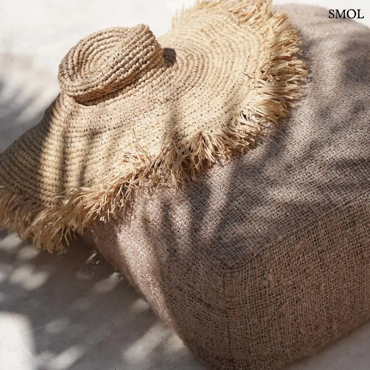 Kézzel szőtt, natúr barna szalmakalap széles, rojtos karimával, barna puffon