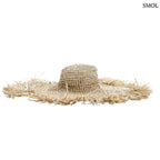 Kézzel szőtt, natúr barna szalmakalap széles, rojtos karimával, fehér háttérrel, oldalról