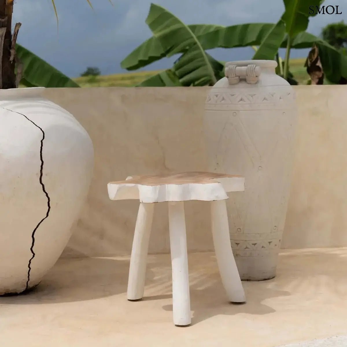 Háromlábú organikus teakfa lerakóasztal natúr fa tetővel és fehér lábakkal, bohém stílusban, teraszon, kaspókkal