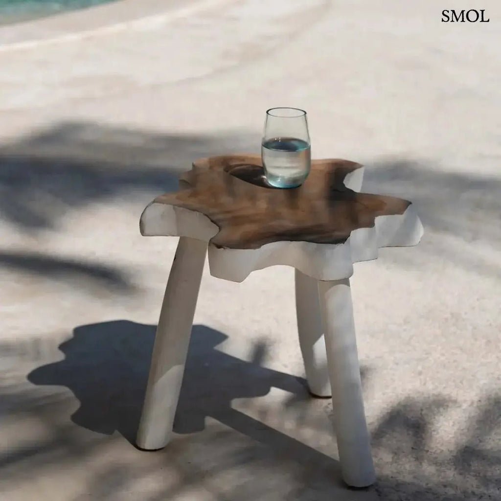 Háromlábú organikus teakfa lerakóasztal natúr fa tetővel és fehér lábakkal, bohém stílusban, vizes pohárral