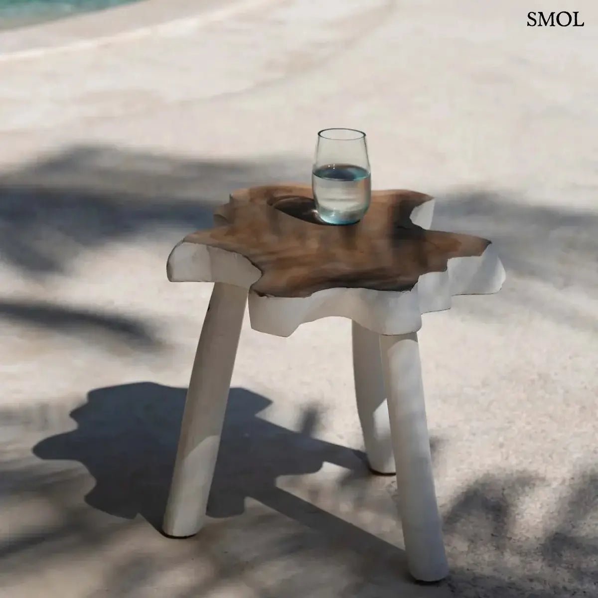 Háromlábú organikus teakfa lerakóasztal natúr fa tetővel és fehér lábakkal, bohém stílusban, vizes pohárral