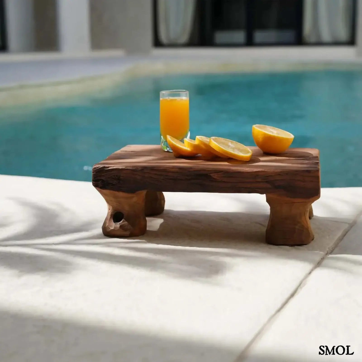 Kézzel faragott, natúr teakfa tálca masszív, rusztikus lábakkal medencével háttérben