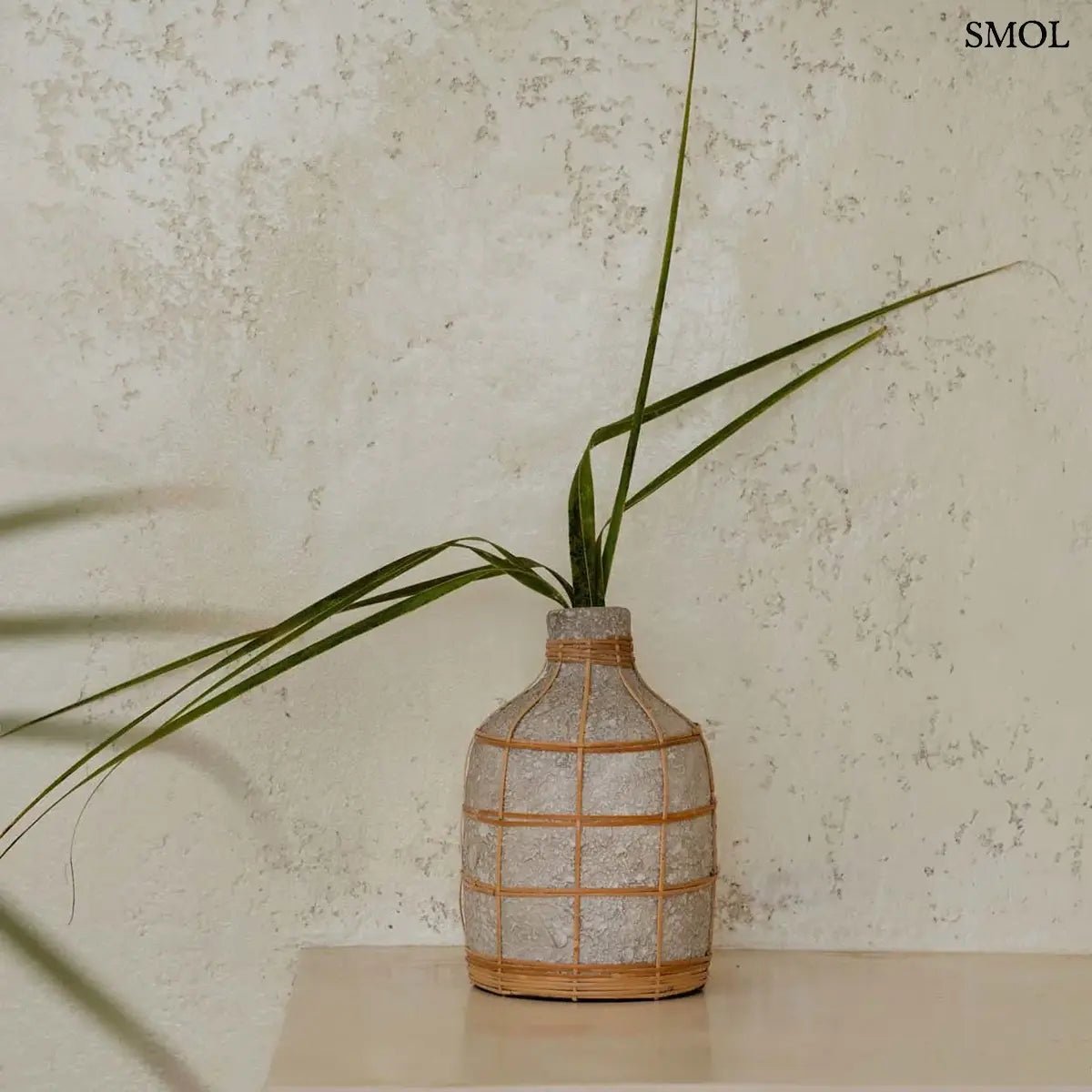 Beton hatású dekor váza kézzel szőtt rattan díszítéssel és rusztikus terracotta felülettel, zöld levéllel