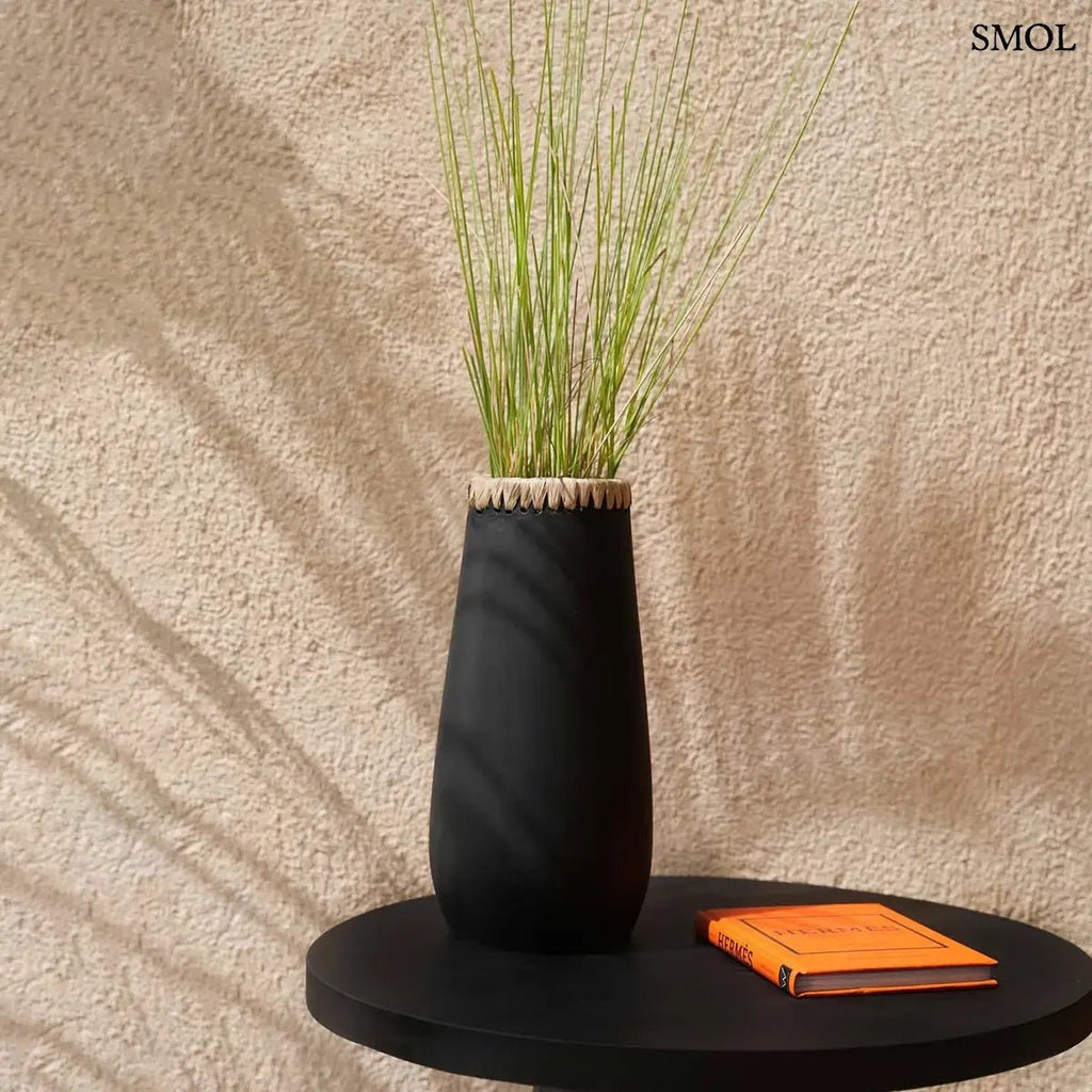 Modern fekete terrakotta váza natúr raffia peremmel, henger alakú kézműves lakásdekoráció egzotikus és minimál stílusú terekbe, fekete asztalon, könyvvel