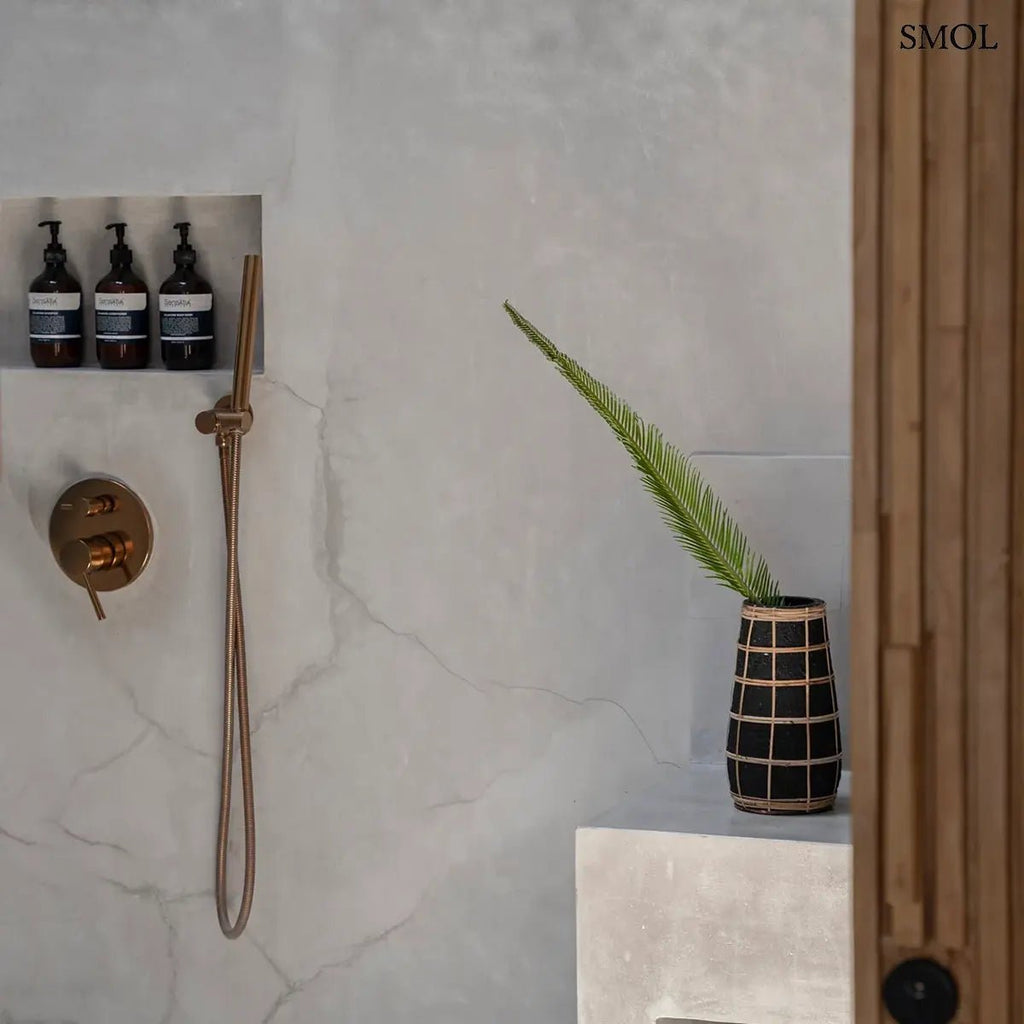 Fekete színű, rusztikus felületű terrakotta váza, amelyet világosbarna, kézzel font rattan rácsozat díszít, fürdőszobában