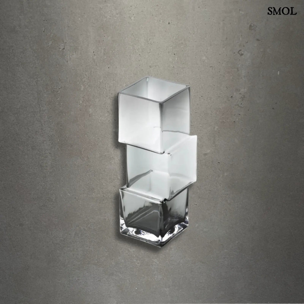 Függőlegesen elrendezett, három kocka alakú sötétszürke üveg váza, szürke háttérrel