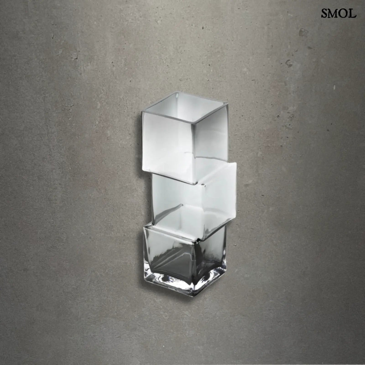 Függőlegesen elrendezett, három kocka alakú sötétszürke üveg váza, szürke háttérrel