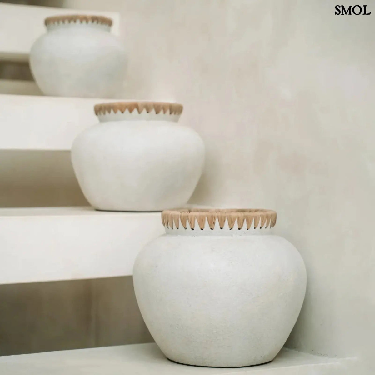 Rusztikus natúr terrakotta váza kézzel font raffia díszítéssel a peremén, lépcsőn