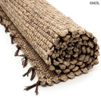 Kézzel szőtt, világosbarna vízijácint szőnyeg, jellegzetes fonott textúrával és sötétebb, csomózott rojtos szegéllyel, feltekerve